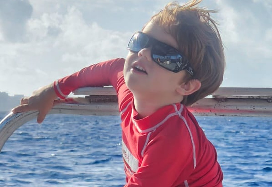 A young guest in a red rash guard enjoying a family boat day with DNS Diving in Grand Cayman